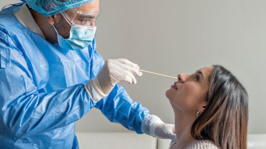 Zdravstveni delavec testira mlado pacientko na okužbo z virusom SARS-CoV-2.