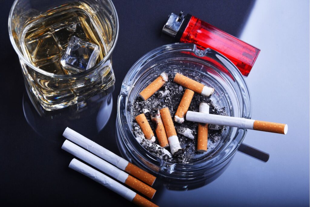 Pepelnik s cigareti, ob njem je vžigalnik in kozarec viskija