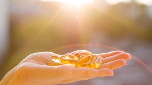 Sonce v ozadju, ženska roka s kapsulami vitamina D v ospredu, konceptualna fotografija